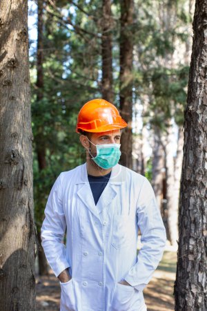 Téléchargez les photos : Technicien avec manteau de laboratoire blanc casque de protection et masque chirurgical isolé sur fond nature - en image libre de droit