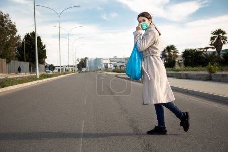 Photo for Woman crosses the street with a blue shopping bag - Royalty Free Image