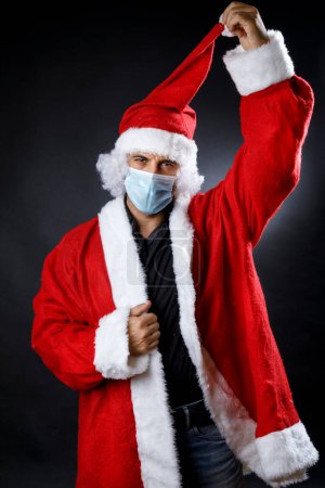 Photo for Santa Claus with surgical mask pulls up his hat, isolated on neutral background - Royalty Free Image