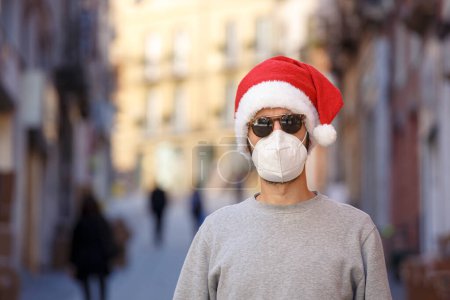 Photo for Man with Santa Claus hat, gray shirt and ffp2 mask in the city center among the shop windows - Royalty Free Image