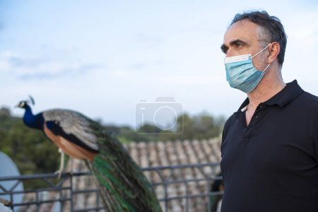 Téléchargez les photos : Homme en vacances habillé décontracté se détend sur une terrasse d'une résidence avec masque facial - en image libre de droit