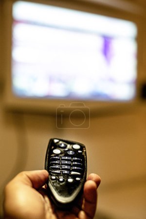 Téléchargez les photos : Télécommande au premier plan tenue par une main et un téléviseur flou en arrière-plan - en image libre de droit
