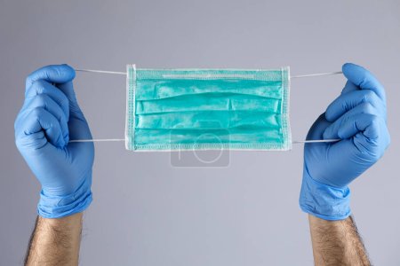 Photo for Detail of latex gloves holding a protective face mask in hand, isolated on light background - Royalty Free Image
