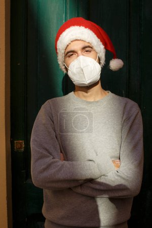 Foto de Hombre joven en sombrero de Navidad y máscara médica, concepto de Navidad - Imagen libre de derechos