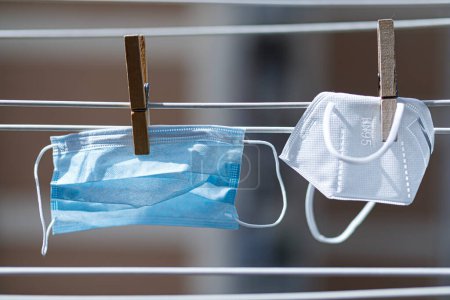 Foto de Máscara facial blanca y máscara quirúrgica azul claro colgado en los hilos con pinzas de ropa para secar - Imagen libre de derechos