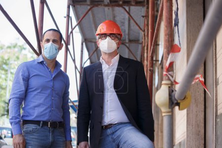 Foto de Ingeniero y gerente de obra en el trabajo con casco naranja y máscara quirúrgica mirar a la distancia - Imagen libre de derechos
