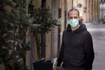 Téléchargez les photos : Homme se promenant dans la ville déserte avec masque et sweat-shirt noir - en image libre de droit