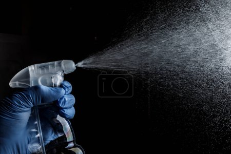 Foto de Hombre rociando desinfección sobre un fondo negro. - Imagen libre de derechos