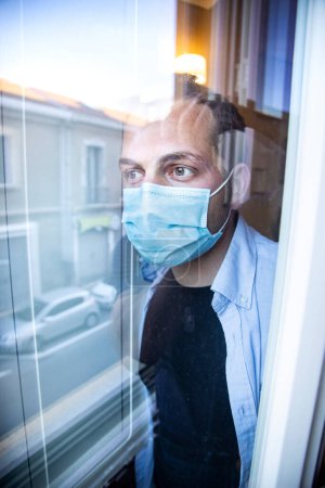 Photo for Man in medical mask and protective gloves looking out window - Royalty Free Image
