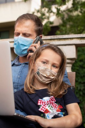 Téléchargez les photos : Père avec fille dans des masques à l'aide d'un ordinateur portable - en image libre de droit