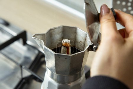Foto de La mano abre la tapa de la cafetera con café saliendo sobre la estufa - Imagen libre de derechos