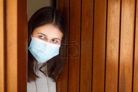 Photo for Girl with facial mask looks sad looking out the front door of the house - Royalty Free Image
