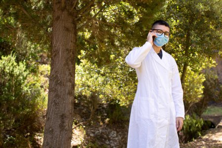 Téléchargez les photos : Homme en costume médical et masque médical de protection parlant téléphone à l'extérieur - en image libre de droit