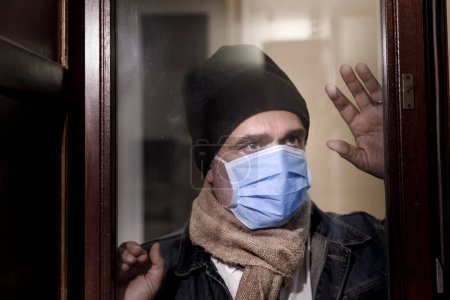 Photo for Man with protective face mask and cap, looks through a glass - Royalty Free Image