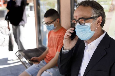 Foto de Hombres en máscaras protectoras con teléfonos móviles en la calle - Imagen libre de derechos