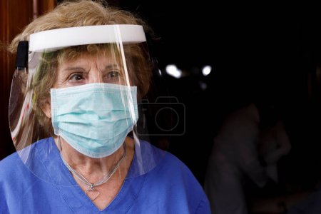 Téléchargez les photos : Médecin femme âgée avec masque facial et bouclier protecteur, isolé sur fond noir - en image libre de droit