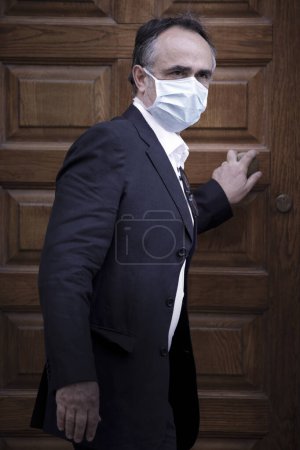 Photo for Portrait of middle-aged man in jacket with protective face mask in front of a doorway - Royalty Free Image