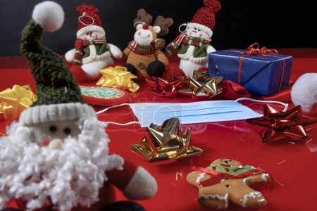 Téléchargez les photos : Masque chirurgical au milieu de nombreux éléments et décorations de Noël sur une table rouge - en image libre de droit