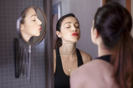 Photo for Beautiful white girl with black hair wears makeup in the bathroom mirror of her house - Royalty Free Image