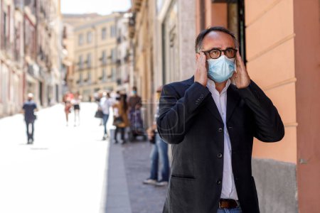 Téléchargez les photos : Homme en veste et masque chirurgical est debout immobile dans une rue du centre-ville - en image libre de droit