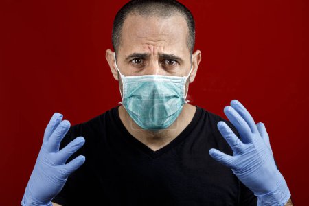 Photo for White man with shaved hair and a black shirt wearing latex gloves wiggling desperate, isolated on red background - Royalty Free Image