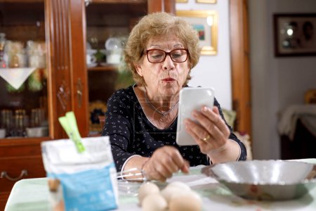 Téléchargez les photos : Femme âgée fait un appel vidéo assis dans le salon de sa maison - en image libre de droit