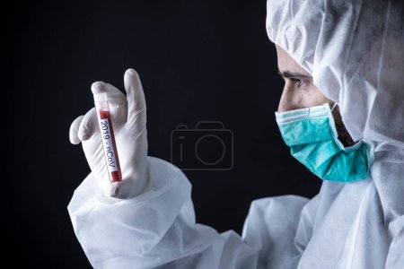Photo for Doctor in protective suit and mask is holding tube for coronavirus blood test - black background - Royalty Free Image