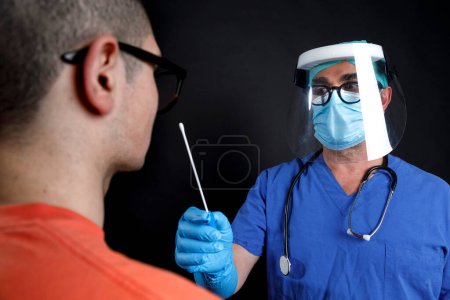 Téléchargez les photos : Médecin avec protection chirurgicale et blouse bleue prenant un tampon pharyngé du patient - en image libre de droit