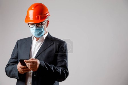 Téléchargez les photos : Ingénieur avec casque et masque de protection, utilise son téléphone portable, isolé sur fond blanc - en image libre de droit