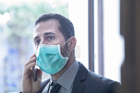 Téléchargez les photos : Homme d'affaires dans le bureau est forcé de travailler avec le masque pour éviter de tomber malade et d'être infecté par le virus - en image libre de droit