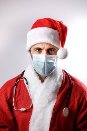 Téléchargez les photos : Père Noël avec masque chirurgical et stéthoscope autour de son cou semble grave et inquiet, isolé sur fond blanc - en image libre de droit