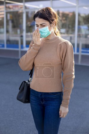 Foto de Mujer con máscara se protege con el brazo de un estornudo - Imagen libre de derechos