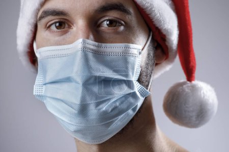 Téléchargez les photos : Santa claus en masque de protection médicale et capuchon sur fond gris. concept de Noël. - en image libre de droit