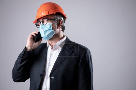 Téléchargez les photos : Ingénieur avec casque et masque de protection, utilise son téléphone portable, isolé sur fond blanc - en image libre de droit