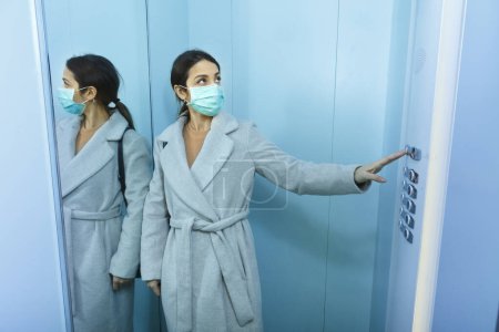 Photo for Brunette girl with coat takes the elevator wearing the protective face mask - Royalty Free Image