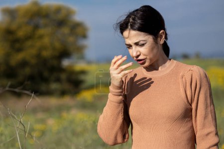 Photo for Brunette girl with orange sweater while sneezing protects herself with her hand, isolated on nature background - Royalty Free Image