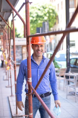 Foto de Ingeniero con hardhat naranja y camisa azul en un contexto de obra urbana - Imagen libre de derechos