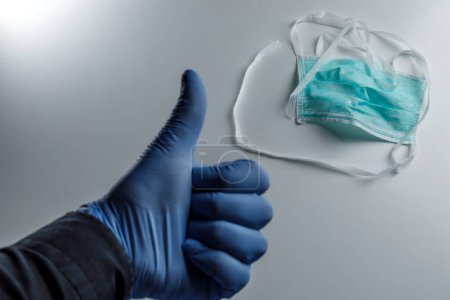 Foto de Mano con guante protector azul hace que el signo ok, en el fondo máscara quirúrgica aislada sobre fondo blanco - Imagen libre de derechos
