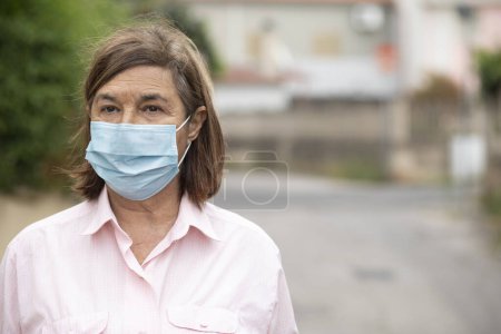 Téléchargez les photos : Femme âgée avec masque de protection debout dehors dans la rue - en image libre de droit