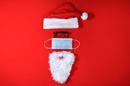 Foto de Composición navideña creativa que recuerda a la cara de Santa Claus con máscara quirúrgica, aislado sobre fondo rojo - Imagen libre de derechos