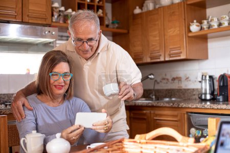 Téléchargez les photos : Couple âgé faire un appel vidéo à la maison cuisine - en image libre de droit