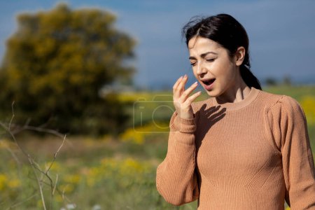 Foto de Morena con suéter naranja mientras estornuda se protege con la mano, aislada en el fondo de la naturaleza - Imagen libre de derechos