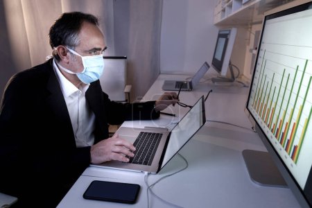 Foto de Hombre usando una máscara quirúrgica que trabaja con el ordenador portátil - Imagen libre de derechos