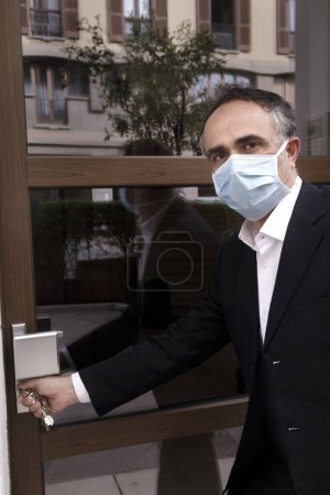 Photo for Man in jacket with protective face mask, is leaving his house worriedly because of the coronavirus - Royalty Free Image