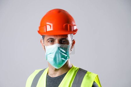Photo for Worker with yellow protective helmet vest and surgical mask, isolated on gray background - Royalty Free Image