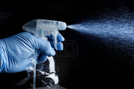 Foto de Mano con guante protector pulveriza el spray con un nebulizador, aislado sobre fondo negro - Imagen libre de derechos