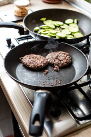 Photo for Hamburger on pan in cooking and next to the other pan with zucchiene - Royalty Free Image