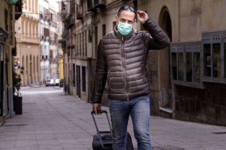 Photo for Man with mask walks in a deserted city in Italy, carrying a suitcase - Royalty Free Image