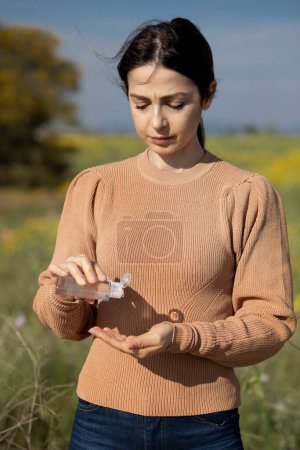 Photo for Brunette girl with orange sweater disinfects her hands with an antibacterial product, isoalta on nature background - Royalty Free Image