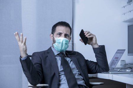 Téléchargez les photos : Homme d'affaires dans le bureau est forcé de travailler avec le masque pour éviter de tomber malade et d'être infecté par le virus - en image libre de droit